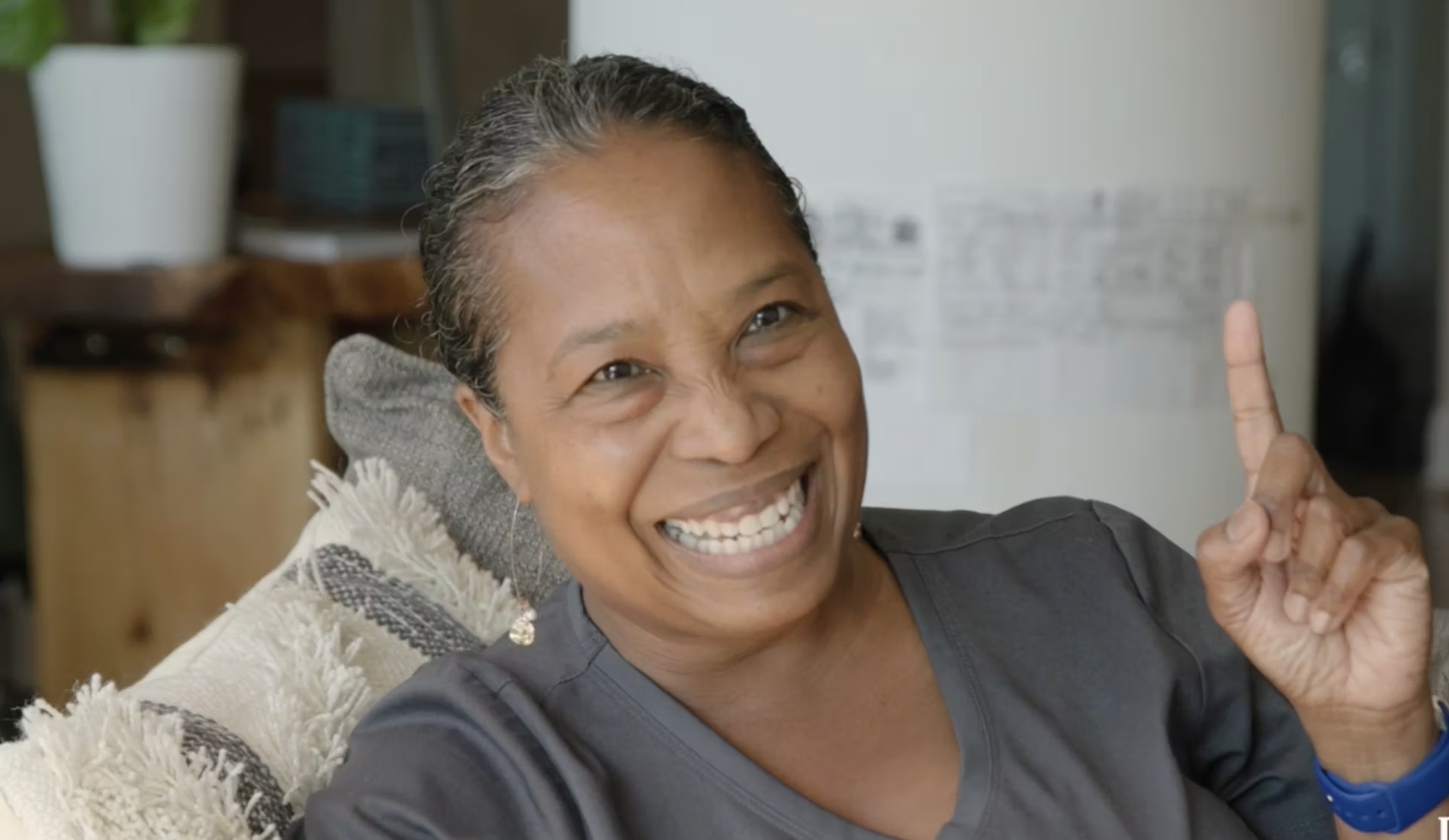 A woman smiling n holding up a finger pointing up.